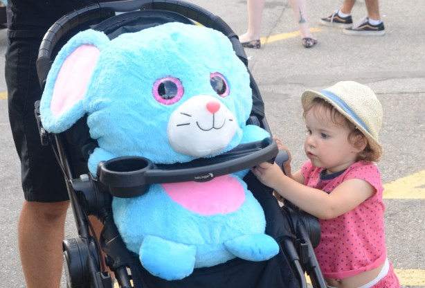 young girl with fedora, helping to clip large blue stuffie into a stroller