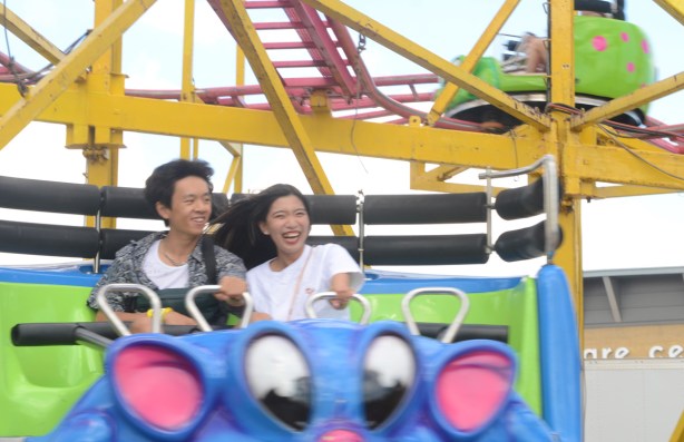 young asian couple enjoying a roller coaster ride, laughing, leaning into each other as they go around a corner