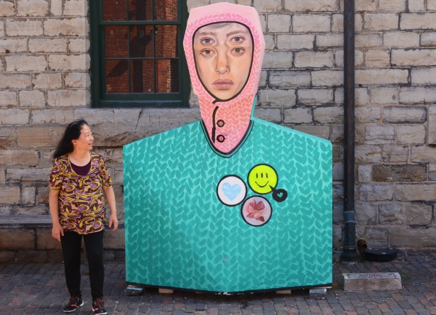 painted sculptures at Distillery District, abstract people shapes, Asian woman standing beside one with pink head scarf, 4 eyes, and a turquoise top