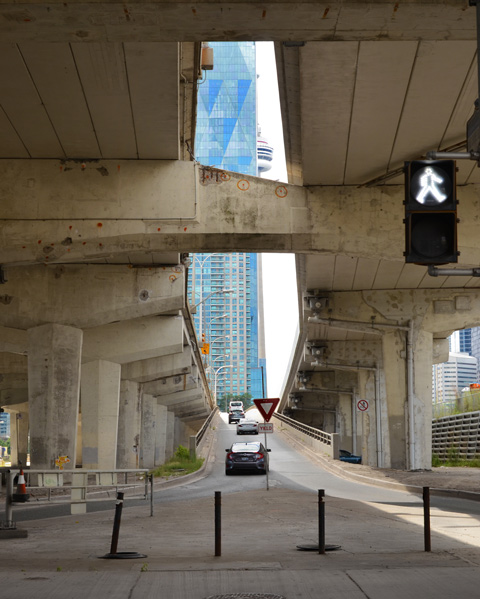 the CN Tower peaks through a gap in the Gardiner Expressway where an on ramp is