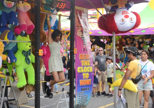 young girl trying to hold onto bar and hang there as long as possible, while a young man with a stuffed banana tries to encourage her