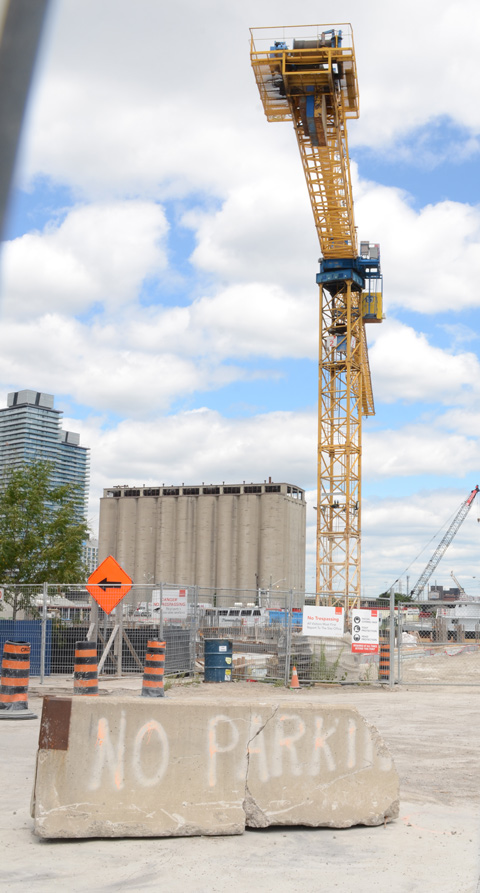 Victory Solya Mills in the background, construction in the foreground, a large yellow crane, a cement barricade spray painted with words no parking