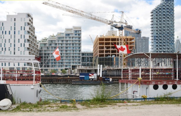 the back ends of two tour boats with Canadian flags flying, end to end, with new condo developments seen across the water