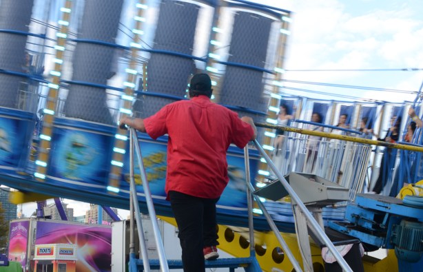 a man watches a spinning ride at the ex, as people are standing as they spin