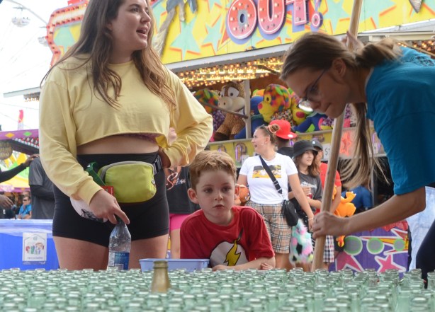 mother and young son at ring toss game, while cne employee sweeps up rings from the ground