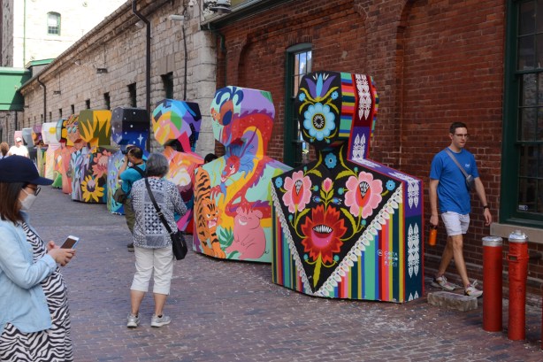 painted sculptures at Distillery District, abstract people shapes, people walking past and looking at them, outdoors