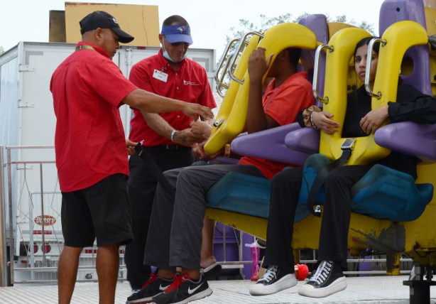 two men working at the cne in red shirts, helping to make sure that young riders are strapped in safely to their seats