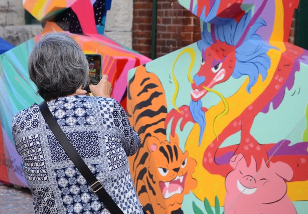grey haired woman taking a picture of painted sculptures at Distillery District, abstract people shapes