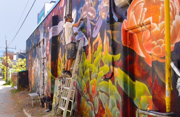 mural part of new dawn project, painting by Nick Sweetman standing on a ladder as he paints bees on the top part of the mural