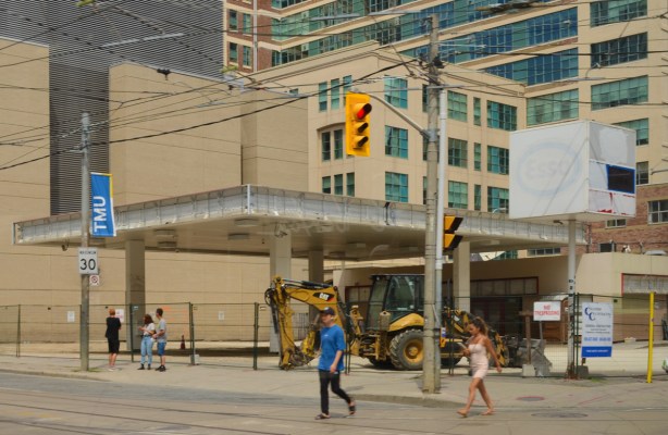northeast corner of Dundas and College. Old gas station that has pumps and most of buildings removed, overhang structure still in place, taller buildings behind