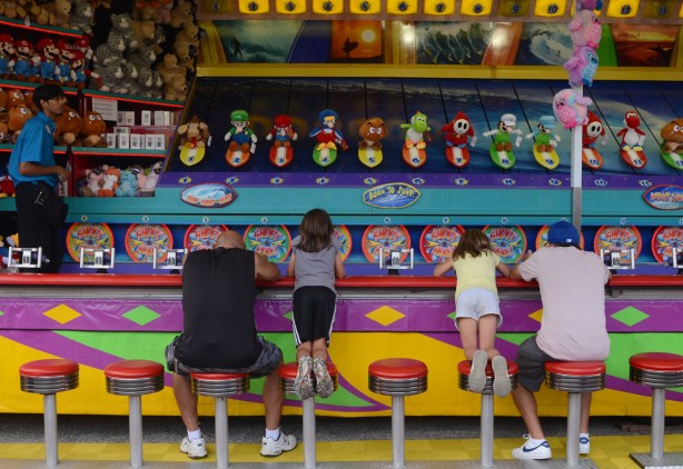 two men with daughters kneeling on stools, playing water shooter game at cne