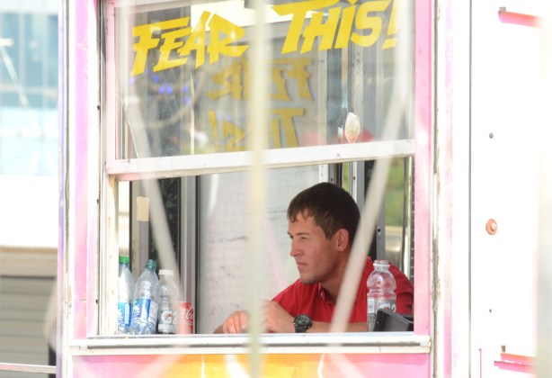a man in a booth with the words fear this in yellow on the window, sitting and looking out at the cne midway