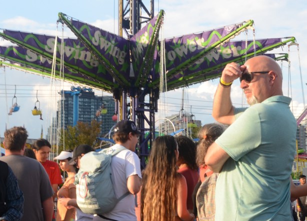 people on the midway, a man shields his eyes from the afternoon sun