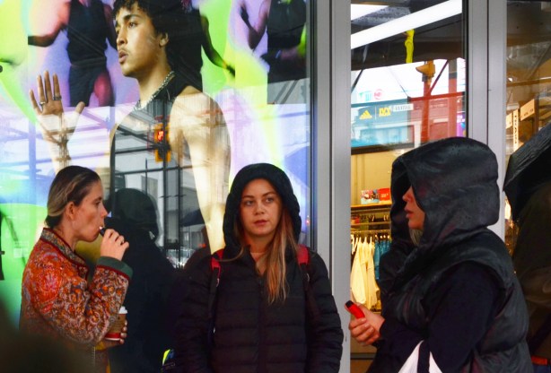 three young woman standing together beside a lit electric advertisement