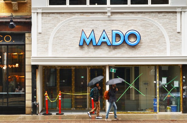 Yonge street on a rainy day, two people with black umbrellas walk past mado, an empty storefront