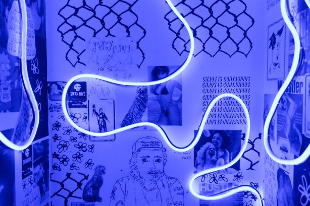 part of washroom wall at Mallo Coffee shop, black and white paper with drawings, images, and words, with a blue neon (led?) light that curves around giving the room an eerie blue glow