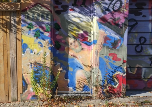painting on a garage of a topless man holding up something very heavy across his back and shoulders, sort of like greek god atlas. 