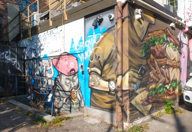 part of an elicser elliott mural on dirty bird chicken and waffle, man in brown eating a very large sandwich on a plate, a smaller man with a drink in his hands