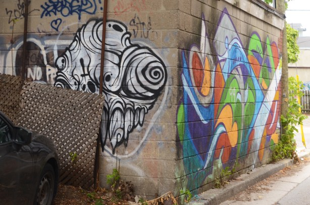 street art on a cement block garage in an alley, a black and white grominator on one side and an abstract of swirls and wavy shapes in multi colours on the other