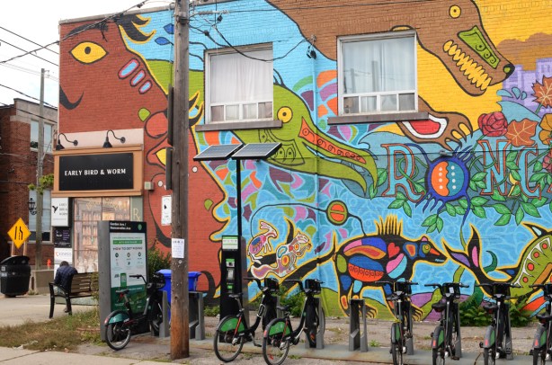 left hand side of new Roncesvalles mural with a large green fish, a blue bird, and a bear, on the side of a brick building