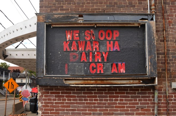 old black sign with red peeling letters that say we scoop kawartha dairy ice cream, some letters missing