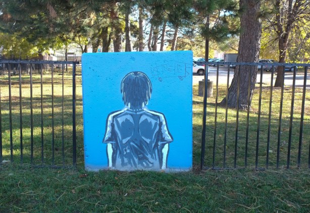 concrete block against a metal fence with simple painting of a person's back