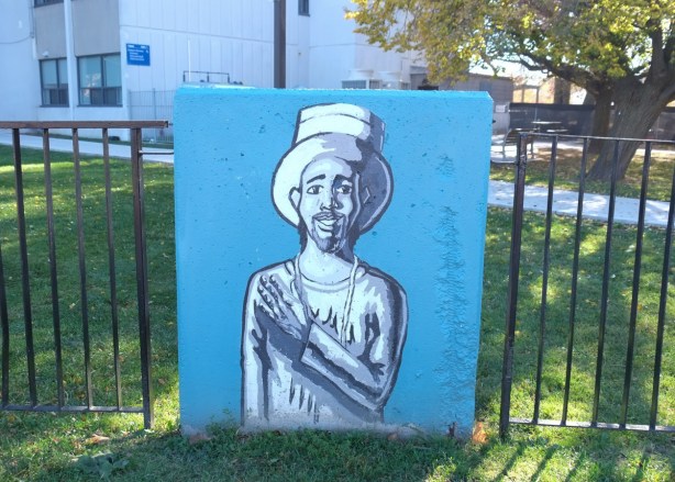 concrete block against a metal fence with simple painting of a person of Caribbean origin, male, wearing oversized heat