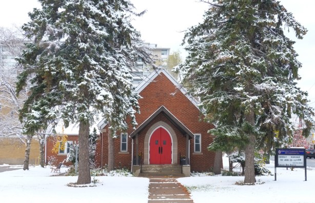 Celebration Presbyterian church on the corner of Coldstream and Bathurst, small brick building, red front door,large pine trees on either side of the front entrance, snow, 