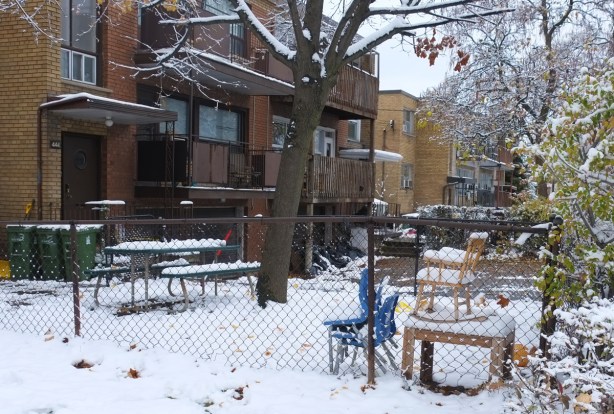 chairs stacked in front of a building on Lawrence, in the snow, beside a chain link fence 