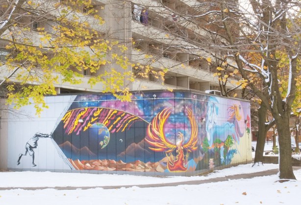 mural at the corner of two walls, a person is peeling back a white curtain to reveal a planet and a phoenix with other things in the mural too, in front of an apartment building in Scarborough