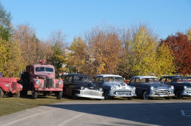 a row of old cars and trucks parked beside a road