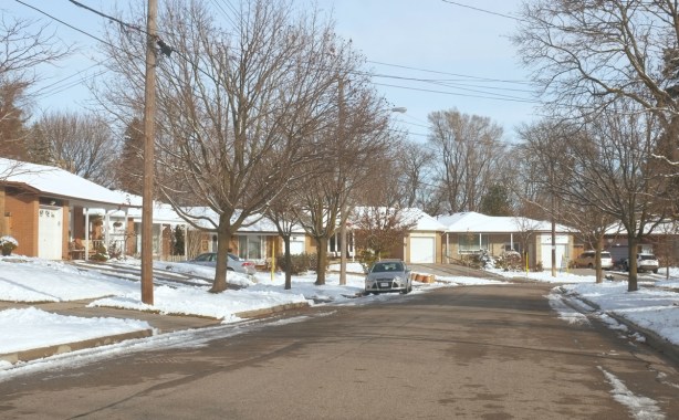 suburban street in winter, single car garages and 1970s bungalows, some trees, one car parked on the street, driveways,