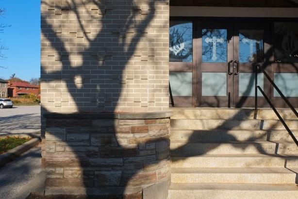 shadow of a large tree on the wall of a church, pattern of crosses in the brickwork, steps up to the door