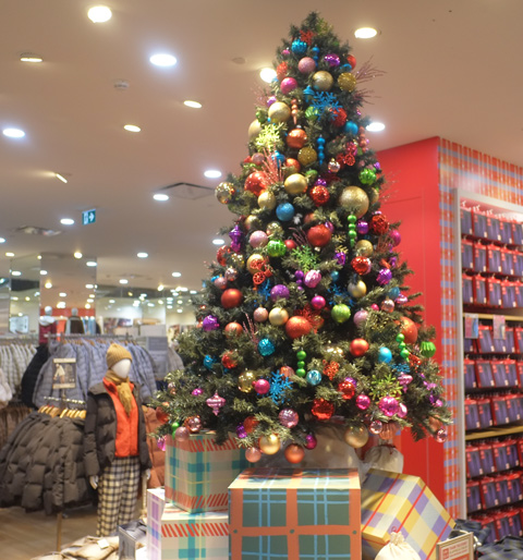 large fake christmas tree with bright coloured balls on it, in uniqlo, a clothing store, with mannequins in winter puffy jackets