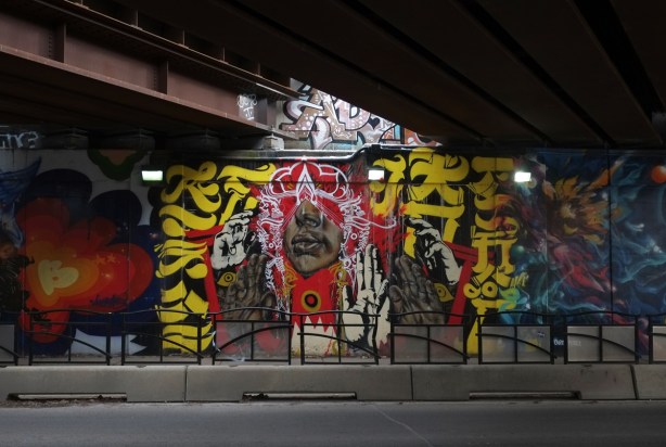street art mural underpass, calligraphy in red and yellow surrounding a black person, face and many black and white hands, 
