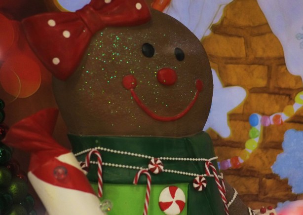 large gingerbread person shape in a christmas display, gingerbread lane, at the Royal york hotel. Large red bow on her head, green glitter on her face, a necklace of candy canes, a green collar on a lighter green top