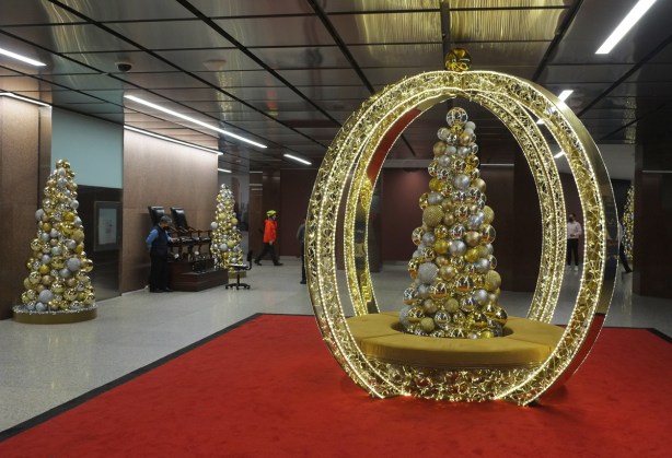 on a red carpet in a large space, a gold decorated christmas tree surrounded by 2 intersecting circular bands of lights so that tree looks like it is in centre of a sphere