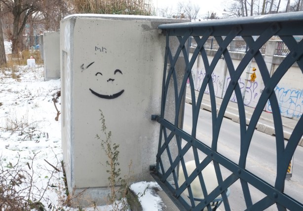 black facial features, closed eyes and smiley mouth, graffiti on concrete railing support