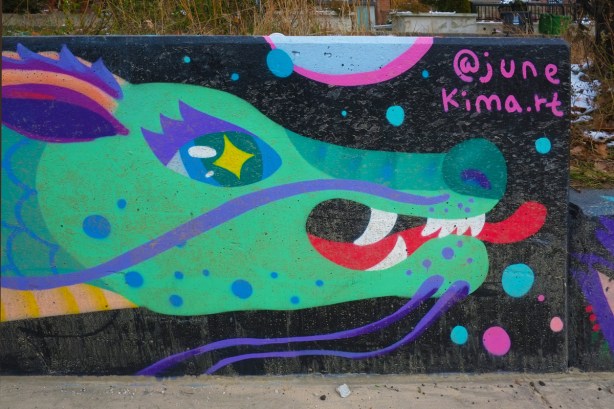 part of a June Jiuen Kim mural of a green gragon head with white teeth, blue spots, blue nose, and blue eyes