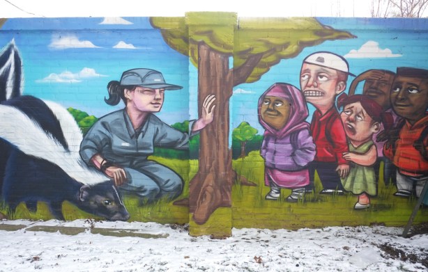 woman in blue uniform sitting on ground beside large skunk, kids watching her