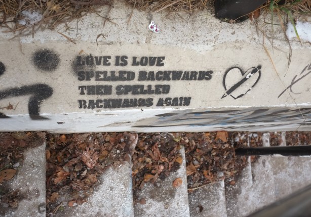 spray painted in black, stenciled text on concrete wall beside outdoor stairwell that says love is love spelled backwards then spelled backwards again