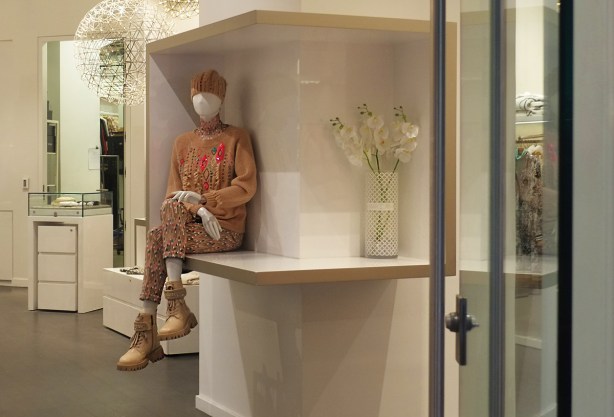 in a store, looking in the door, a faceless mannequin sits on a counter with legs crossed,