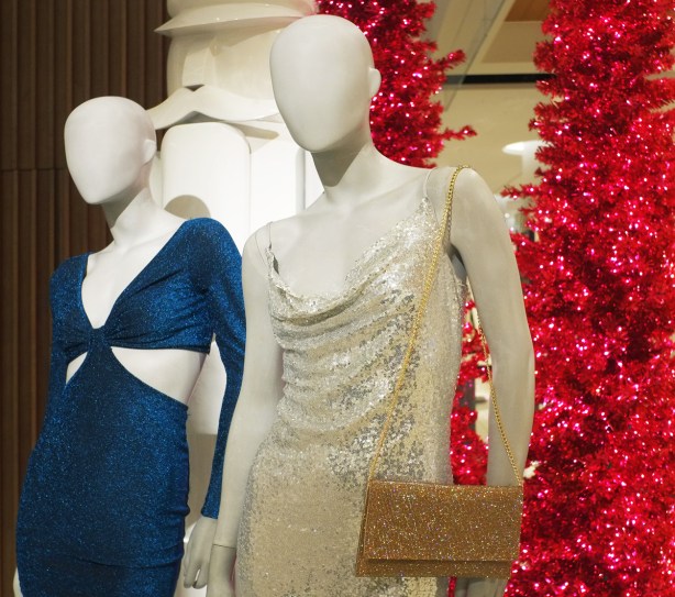 two white female mannequins stand beside a large white nutcracker figure and two very pink magenta fake Christmas trees. One mannequin in a slinky blue dress and the other mannequin in a silvery glittery dress with spaghetti straps. she is holding a gold sparkly handbag