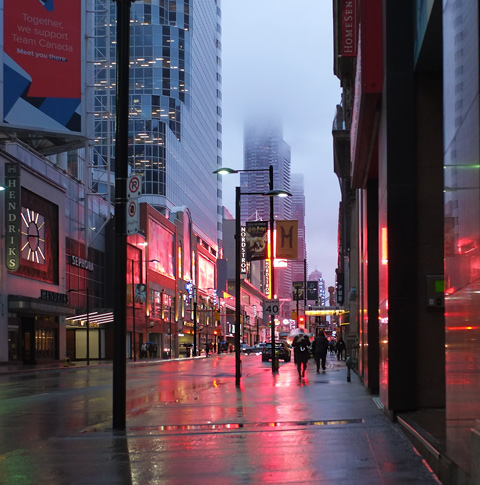 looking north up Yonge street early on a dark morning, lots of red lights reflecting off buildings and pavement from the lights and large signs at Dundas square