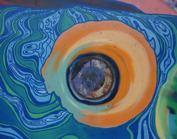 shiny round sculpture embedded in concrete wall that has been incorporated into a street art mural