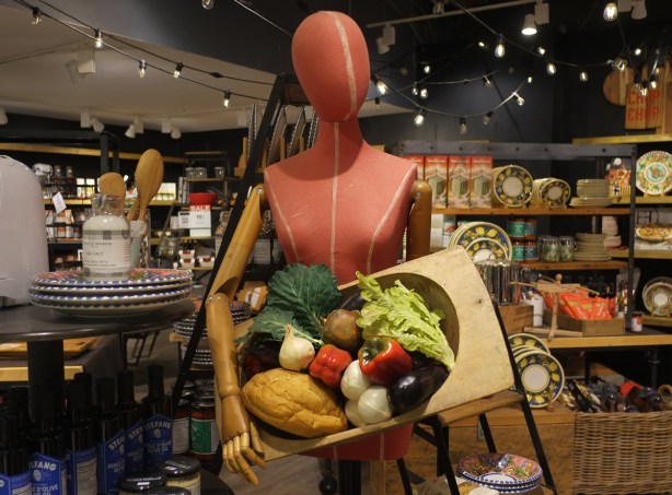 orange coloured faceless mannequin in a store, holding a large bowl of facke food - lettuce, peppers, eggplant,
