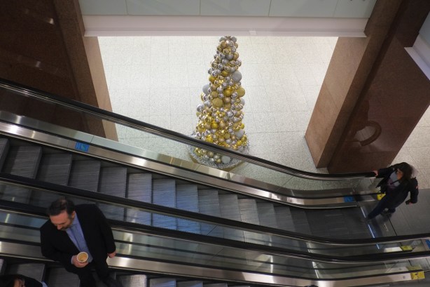 people talking on an escalator, a Christmas tree of gold and silver balls is in the background