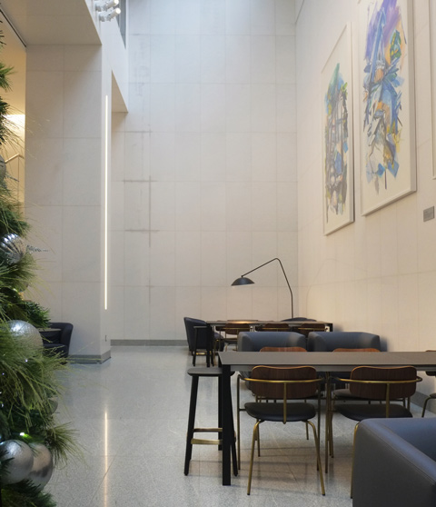 small tables and chairs in a hall space, Christmas tree on one, side, pictures on the wall on the other side,