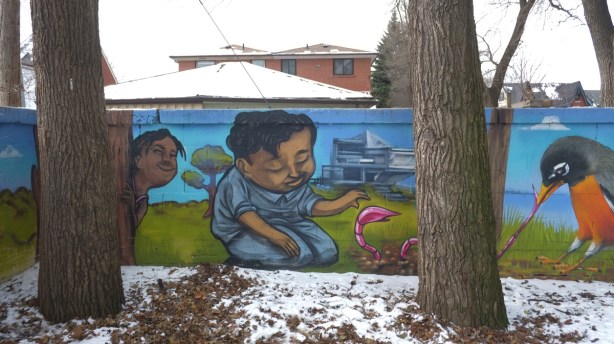 mural, boy outside, kneeling on grass and playing with large pink worm, another boy is hiding behind a tree