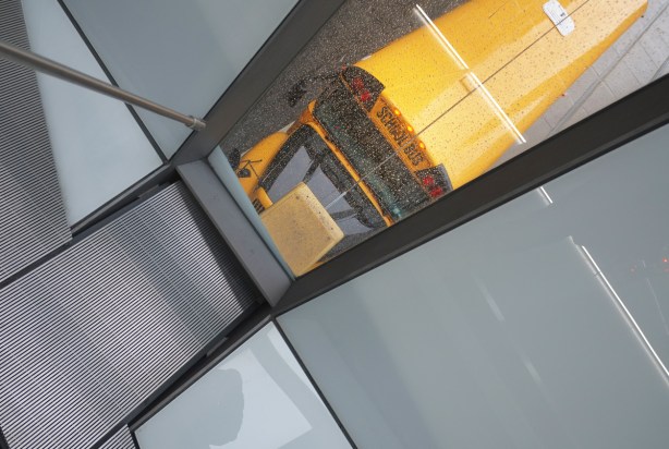 looking out a small window in a pedestrian bridge over queen st., yellow school bus on the street below